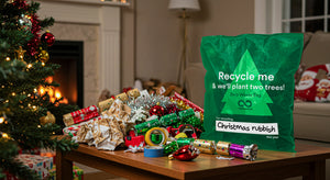 Green recycling bag for Christmas waste with decorative items on a table in a festive living room.