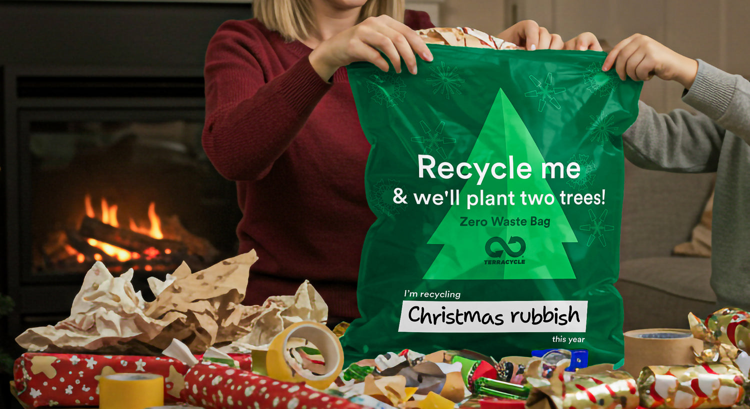Green recycling bag with text held by a person in a festive setting with Christmas decorations.